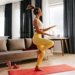Full length of happy young sporty woman in headphones doing aerobics while training at home